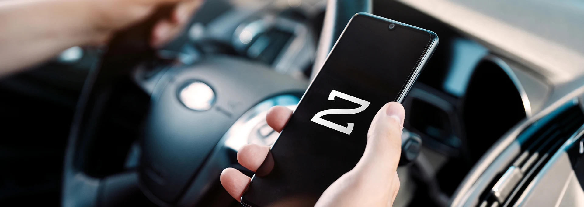 Hand on steering wheel, and holding the Auzo App